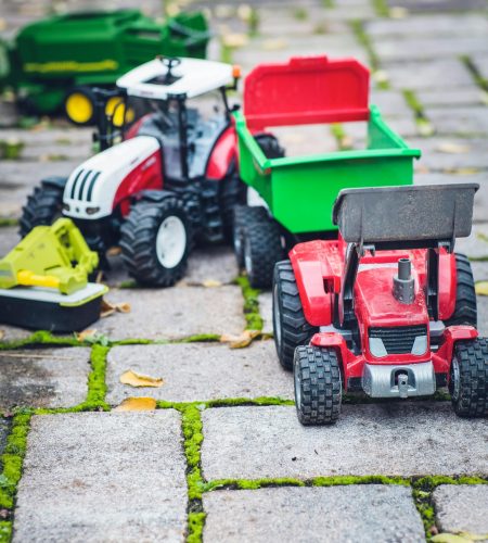 Colorful toy tractors and farming equipment on an outdoor cobblestone path.